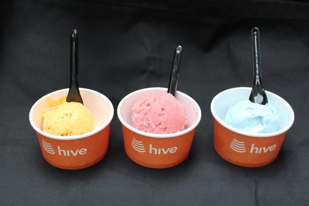 Three branded Hive ice cream tubs with vibrant colour-matched scoops and black spoons