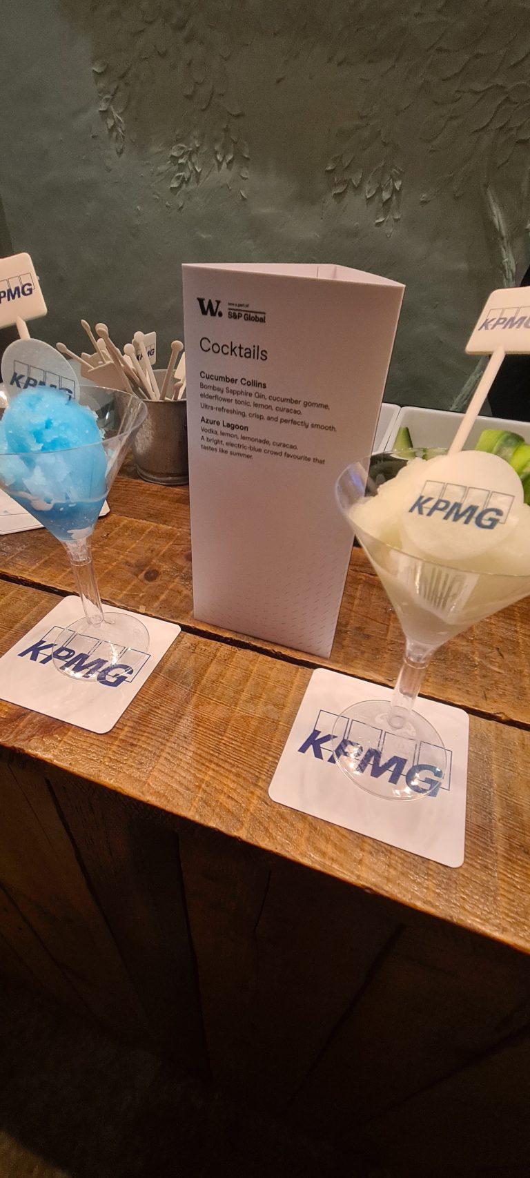 Close-up of bespoke corporate cocktails featuring edible KPMG logo wafer topper, branded coasters, and custom printed cocktail menu card