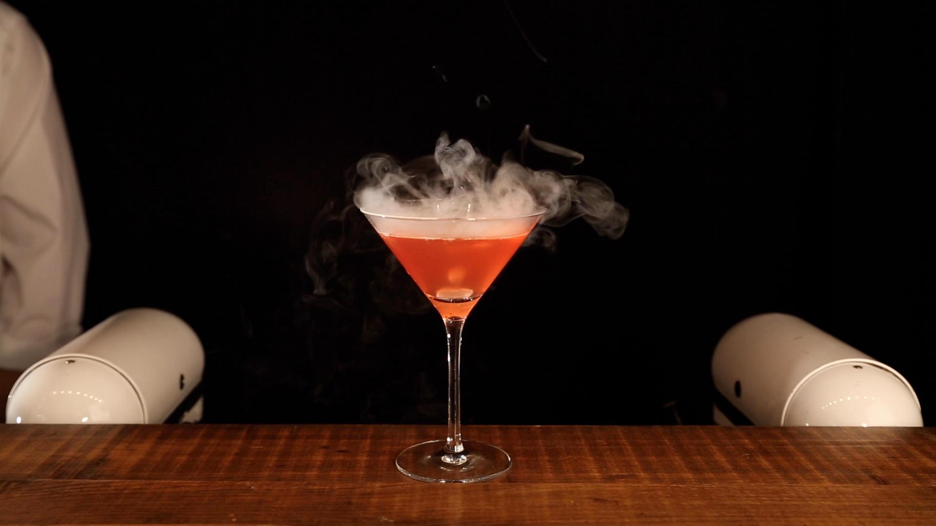 Dry ice smoking red cocktail with dense aromatic vapour clouds on mobile bar counter
