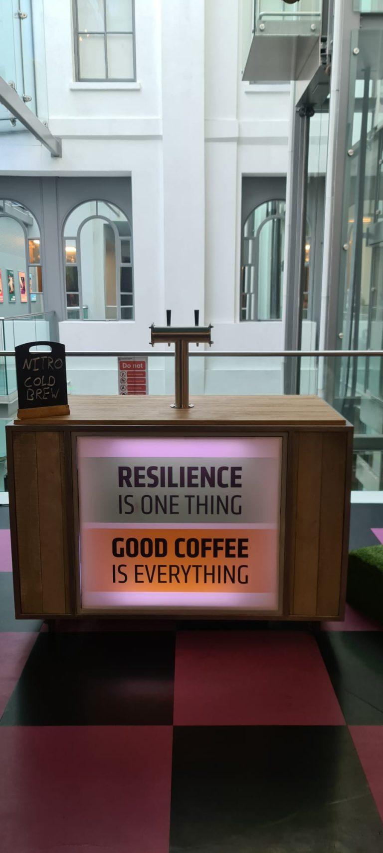 Wooden clad mobile nitro cold brew coffee bar with illuminated branding and draught tap font in a modern corporate atrium