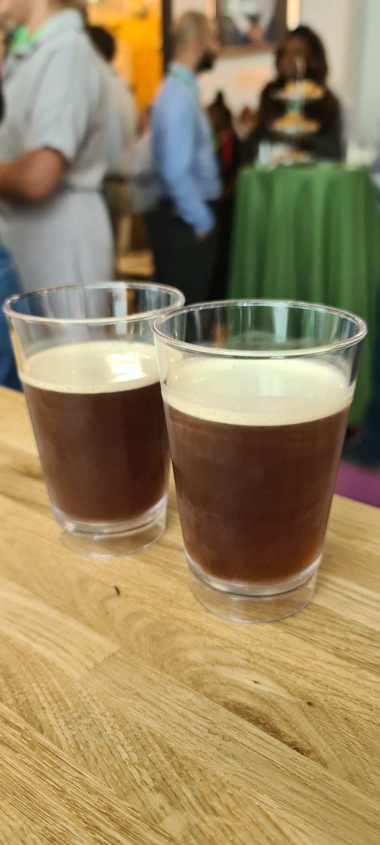 Two glasses of chilled nitro cold brew coffee with velvety creamy heads on a wooden bar counter with event delegates networking
