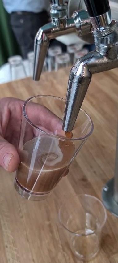 Rich nitro cold brew coffee pouring from a stainless steel draught tap into a clear tumbler on a wooden event bar counter