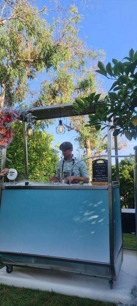 Summer outdoor wedding garden ice cream and lolly cart station adorned with floral arrangements and Edison bulbs