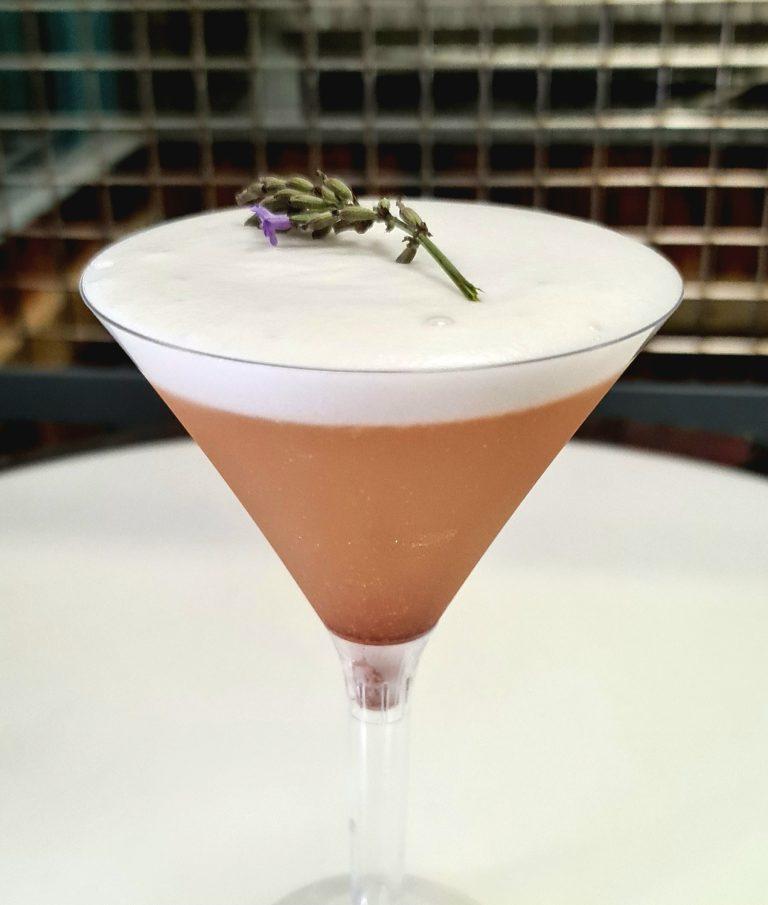 Signature blush pink wedding cocktail in stemmed martini glass with velvet white foam and lavender sprig