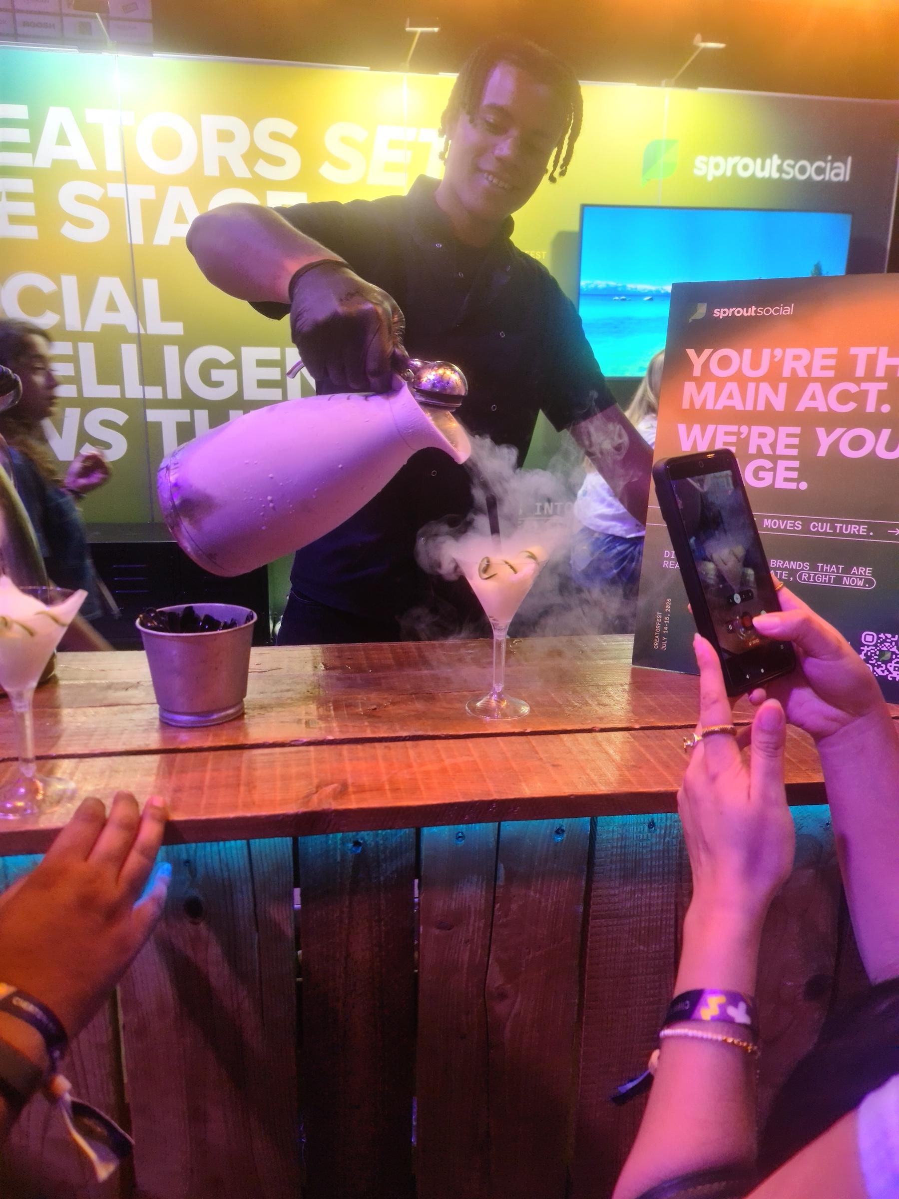 Professional mixologist pouring liquid nitrogen into cocktail glass with dramatic vapour cloud while wedding guests photograph on phones